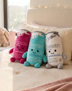 Peach, Winter and Coconut energy can plushies sitting on a cream bed