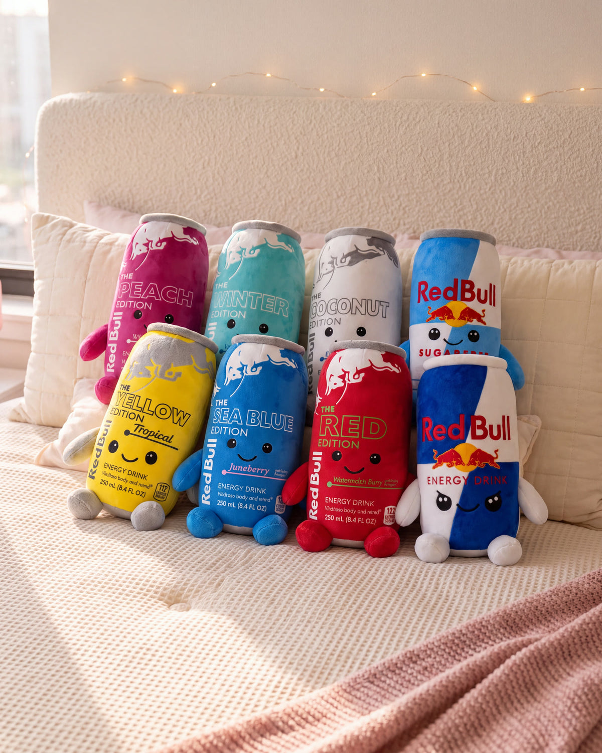 All 8 energy can plushies lined up on a bed