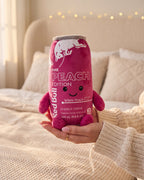 The Peach energy can plushie held up in her hand, soft velvety plush with a smiley face